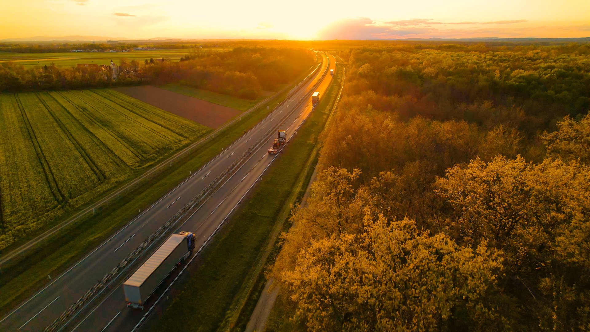 Konvoi av lastebiler på landevei i vakker solnedgang