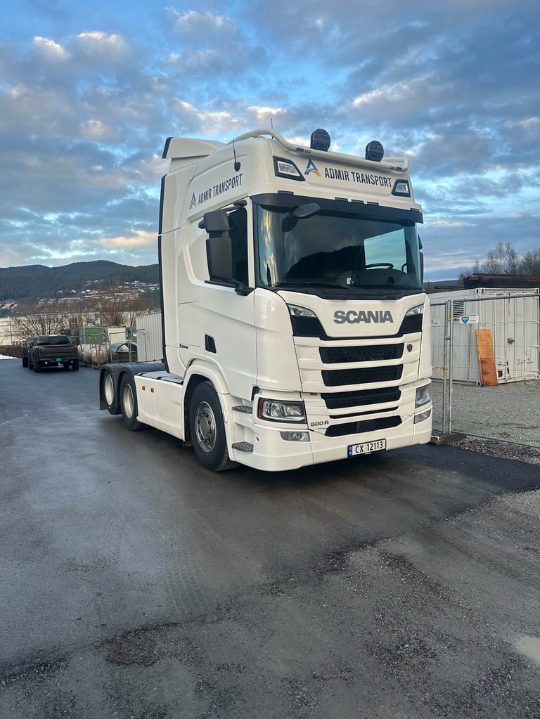 Hvit Scania lastebil med Admin Transport merking parkert ved depot med fjell i bakgrunn
