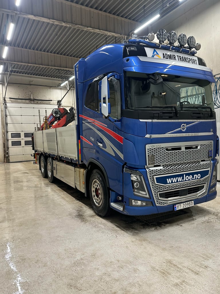 Blå Volvo semi lastebil med Admiral Transport merking parkert i lager med godsplan lastet på tilhenger